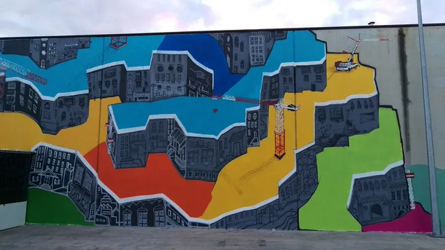 Mural of graphic grey buildings and tower cranes over bold geometric blocks of bright color