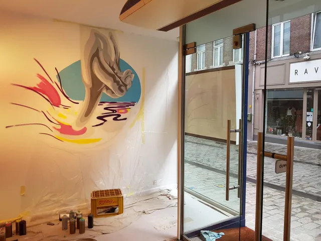 In-progress retail mural depicting a stylized grey hand splashing into vibrant pink and yellow shapes