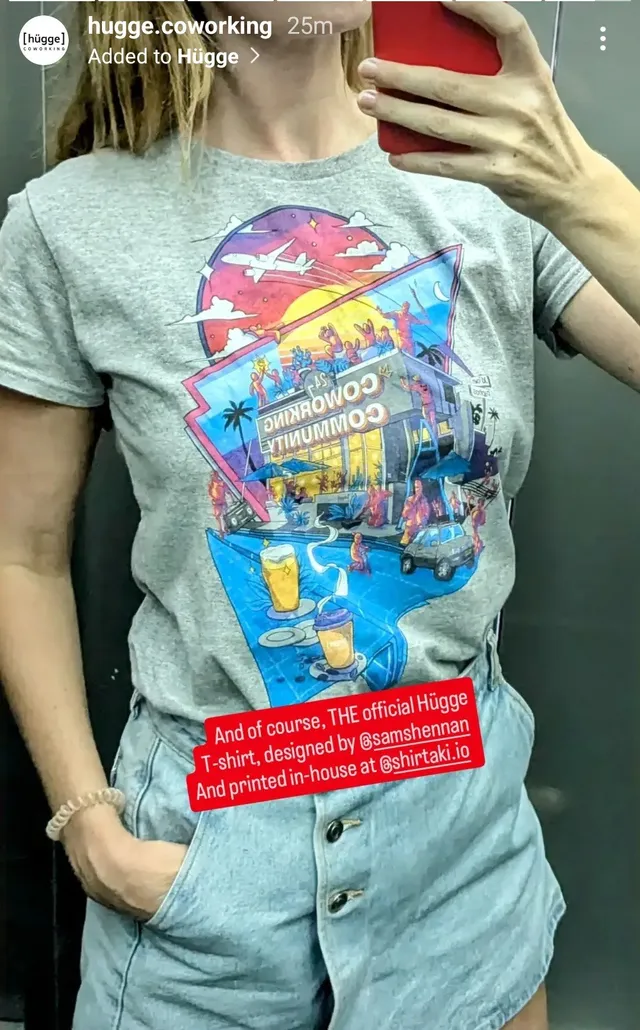 Person wearing a grey t-shirt printed with a colorful, retro illustration of a bustling coworking space
