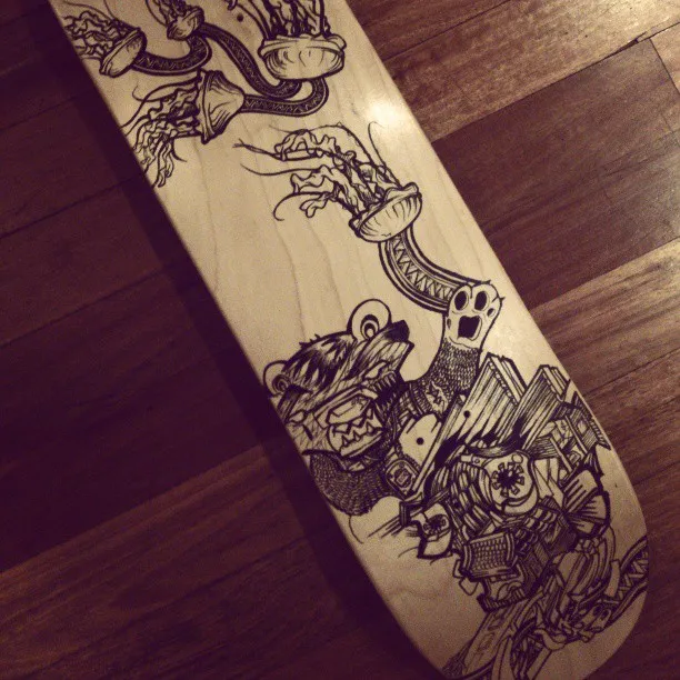 Black ink drawing on a wooden skateboard deck featuring a surreal snarling bear and jellyfish tentacles